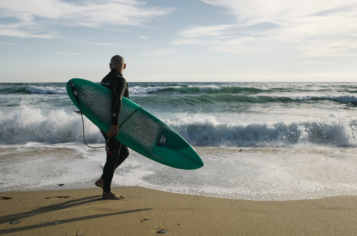 Surfer standing with board on Constantine beach, Cornwall