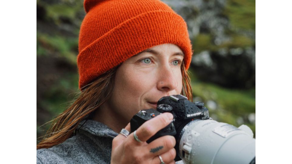 Female Photographer in a red hat uses the OM System OM-1 Mark II